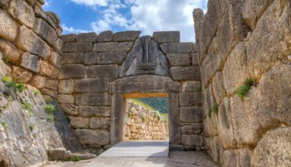 The image shows the Lion Gate at the ancient citadel of Mycenae, featuring large stone blocks and a triangular relief sculpture above the entrance.