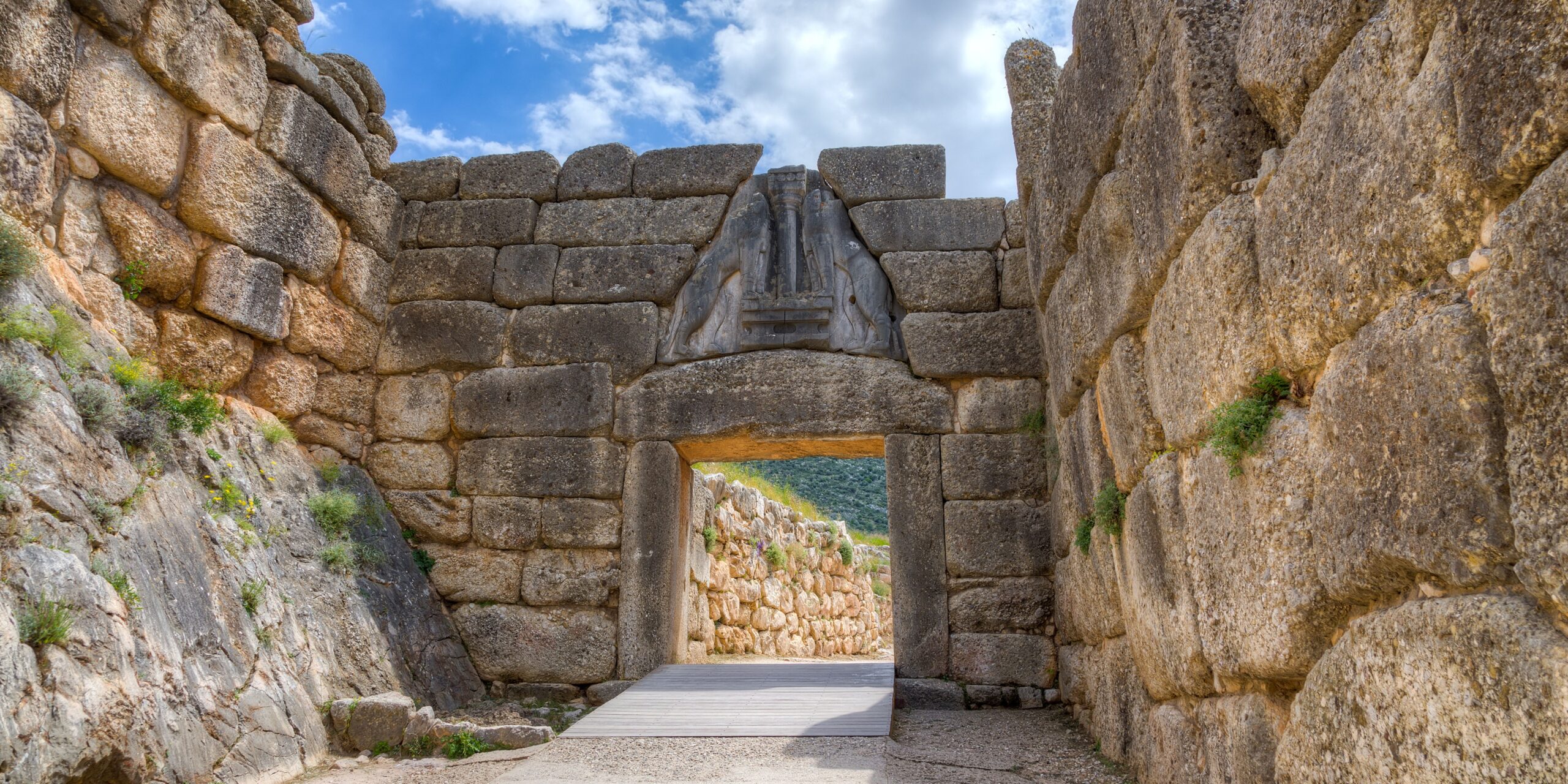 The image shows the Lion Gate at the ancient citadel of Mycenae, featuring large stone blocks and a triangular relief sculpture above the entrance.