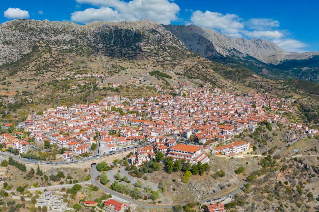 Aerial view of Arachova, Greece, showcasing red-roofed buildings clustered on a mountainside under a partly cloudy sky.
