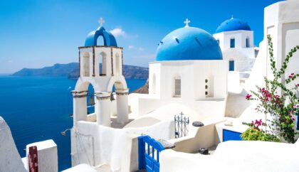 A picturesque view of Santorini featuring iconic white-washed buildings with blue domes overlooking the deep blue Aegean Sea under a clear sky.