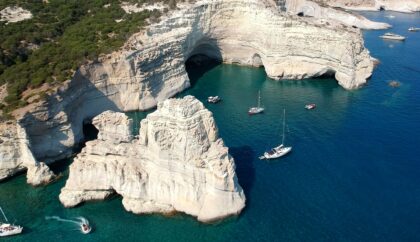 A stunning view of Milos with turquoise waters, dramatic cliffs, and boats anchored near the shore.