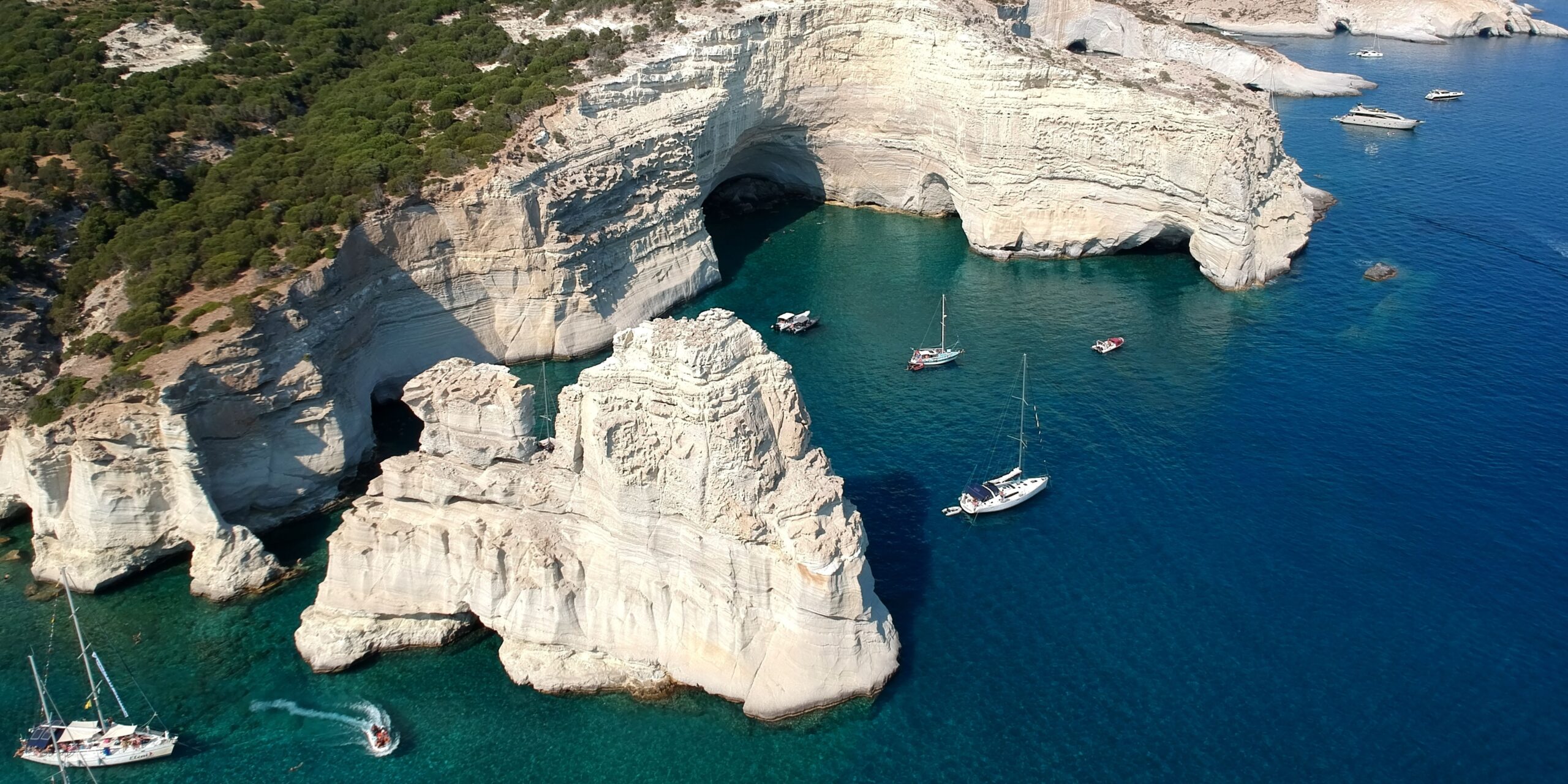 A stunning view of Milos with turquoise waters, dramatic cliffs, and boats anchored near the shore.