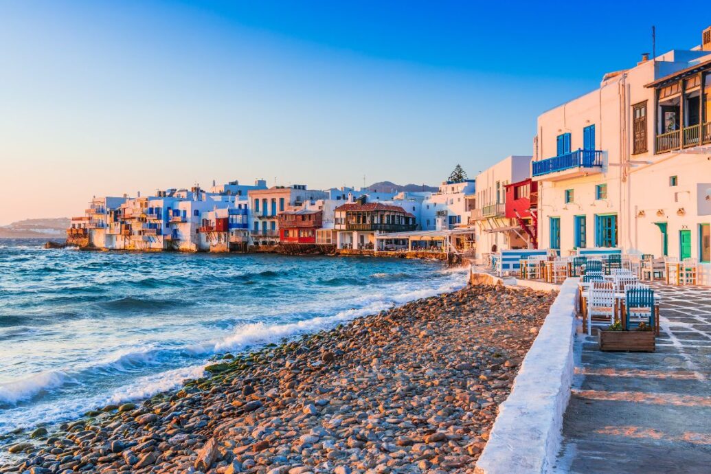 A scenic view of Little Venice in Mykonos, with colorful buildings lining the waterfront and the sea gently lapping at the rocky shore_Mykonos Greece Vacation