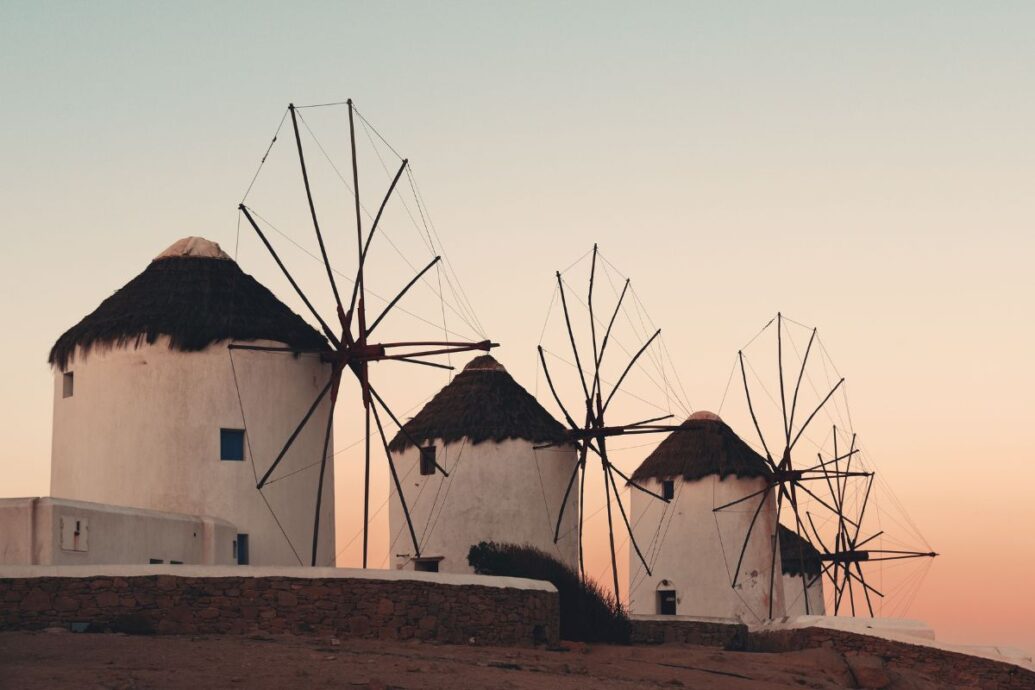 The iconic windmills of Mykonos silhouetted against a serene sunset sky_Mykonos Greece Vacation