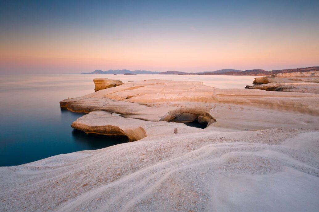 Sarakiniko Beach at sunset, showcasing the unique white volcanic rock formations blending into the calm sea.