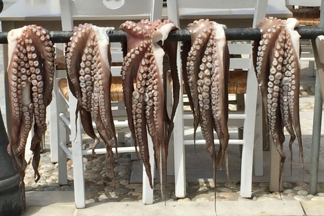 Fresh octopus tentacles hanging to dry in the sun outside a taverna in Naxos, highlighting the island's traditional seafood offerings.