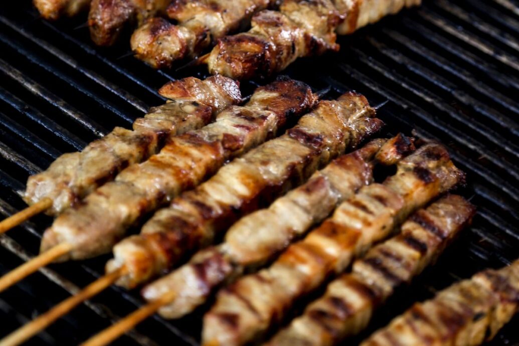 The image shows several skewers of grilled meat, likely souvlaki, cooking on a grill. The meat is charred and golden-brown, suggesting it's well-cooked and ready to be enjoyed.