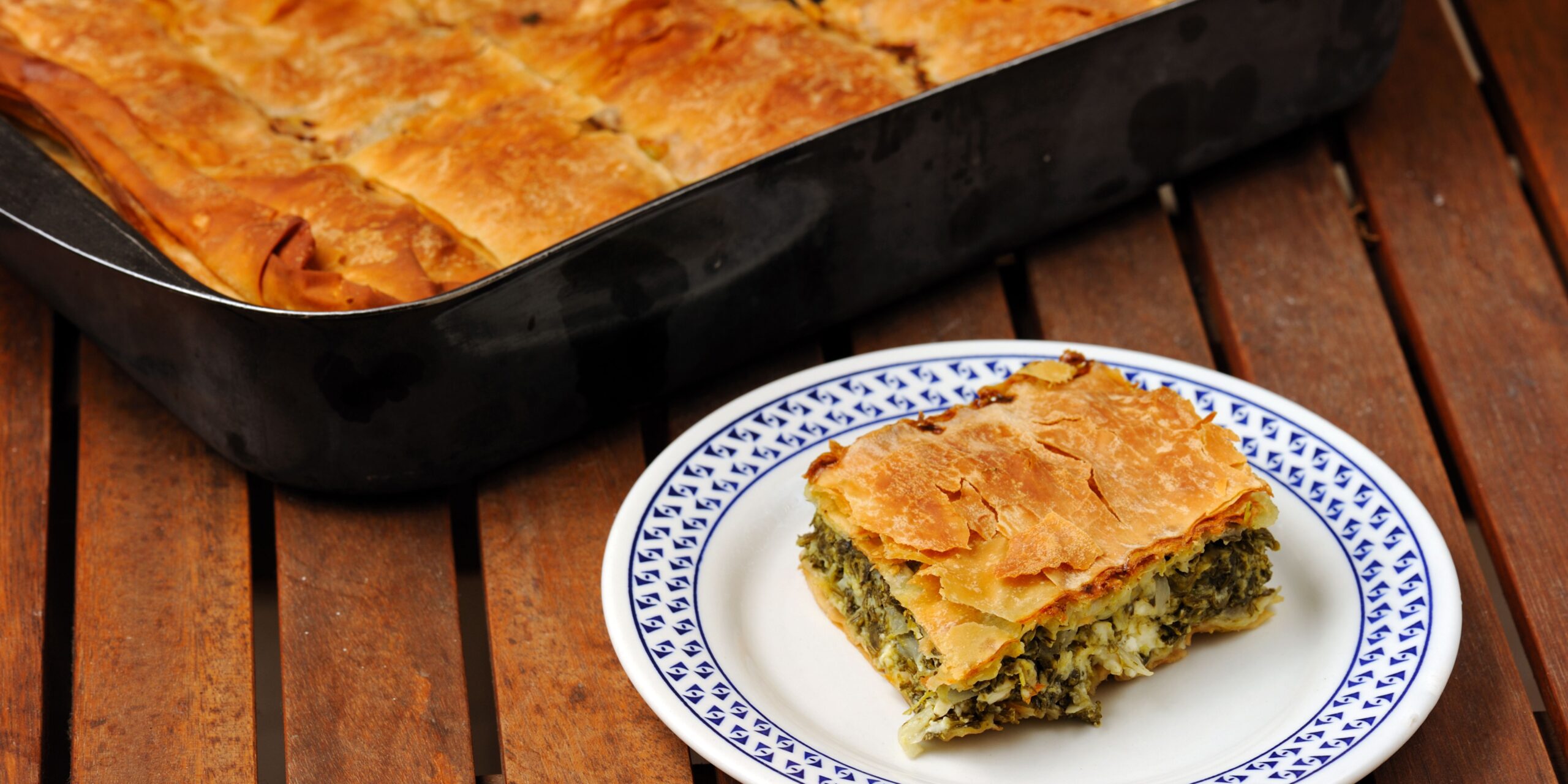 The image shows pieces of spanakopita, a traditional Greek savory pie made with flaky filo pastry and filled with spinach and cheese. The golden-brown, crisp layers are visible, giving the dish a mouthwatering appearance.