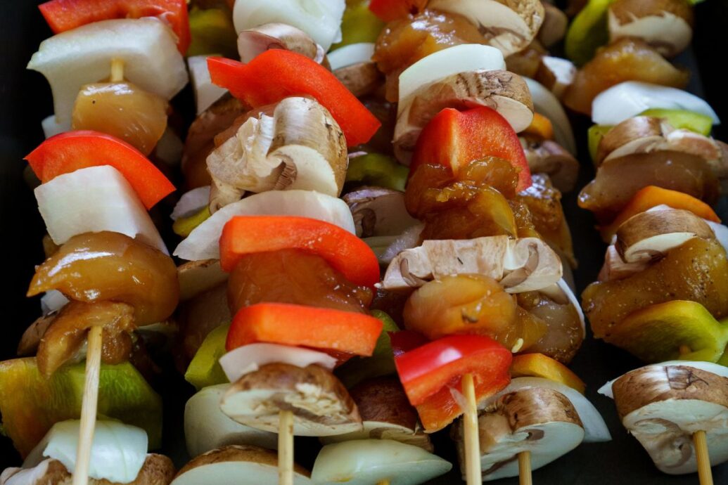 The image shows skewers with a mix of vegetables and marinated meat, including bell peppers, onions, and mushrooms, ready for grilling.