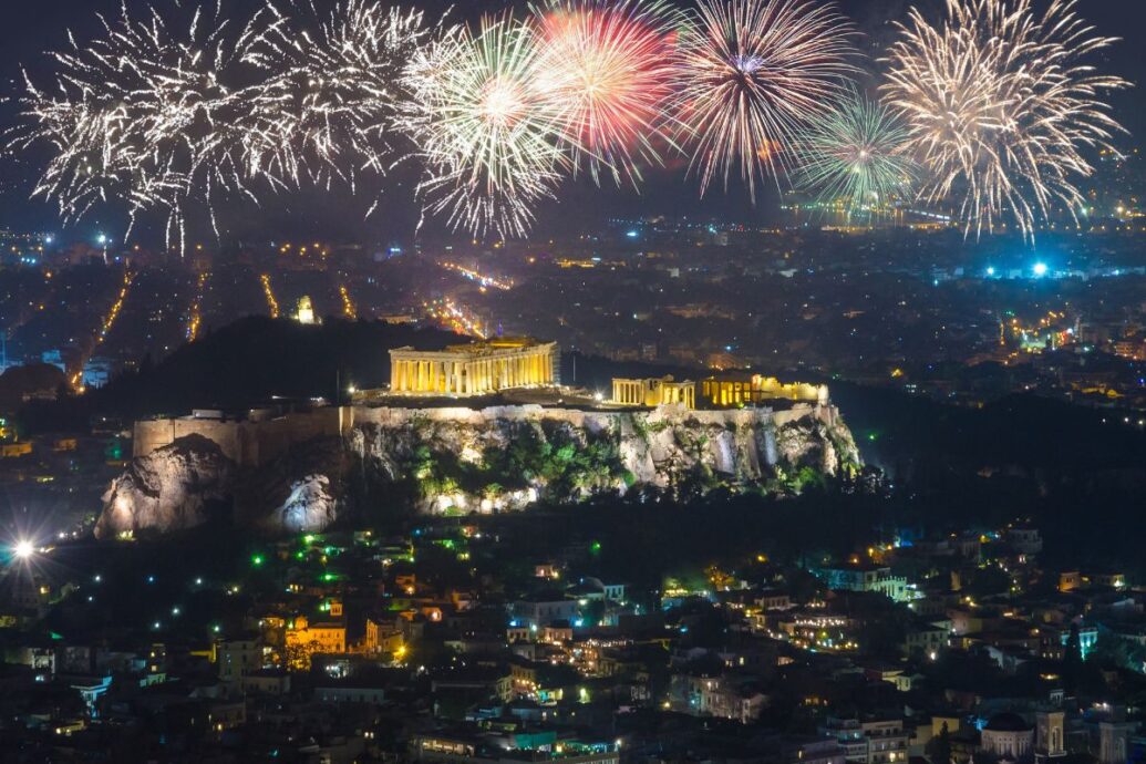 A vibrant New Year's celebration in Athens, with fireworks illuminating the night sky above the illuminated Acropolis, creating a festive atmosphere over the city.