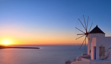 A windmill overlooking the sea during a peaceful sunset, with vibrant hues of orange and blue in the sky.