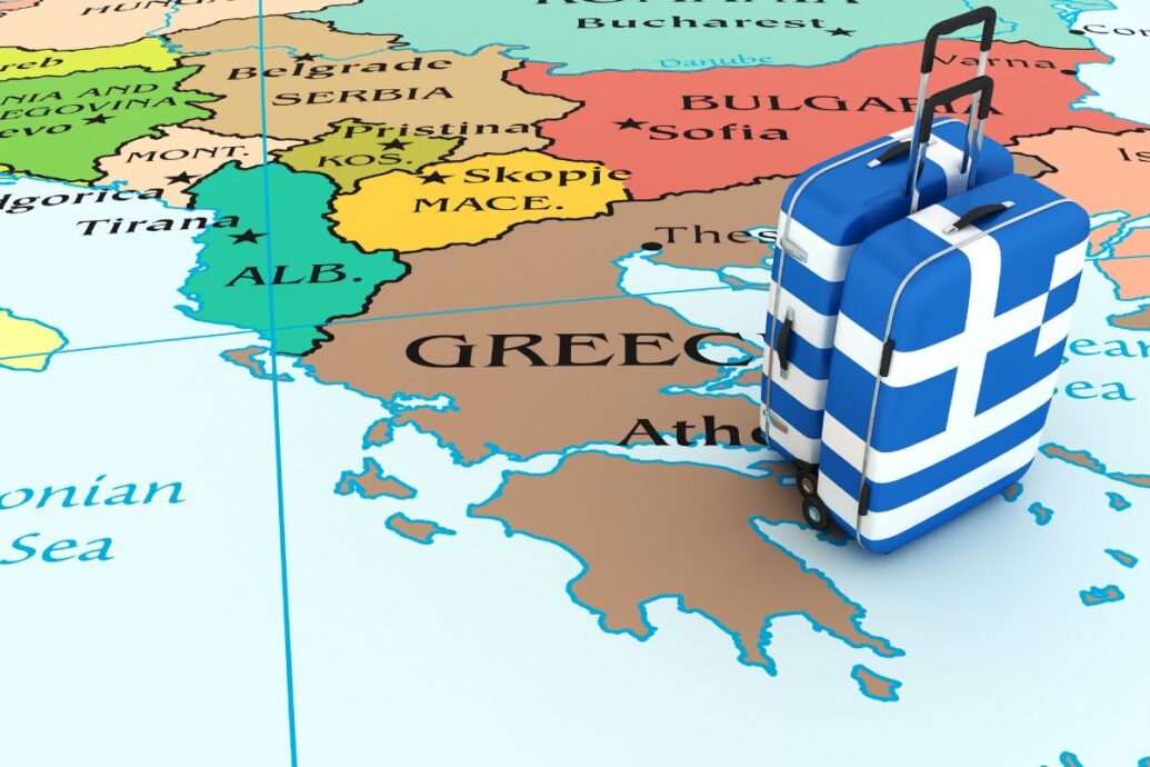 A map of southeastern Europe highlighting Greece with two suitcases styled with the Greek flag placed over the country.