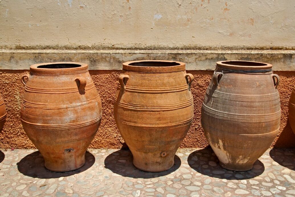 A row of large, traditional Greek terracotta pots displayed against a textured wall, showcasing ancient pottery craftsmanship.