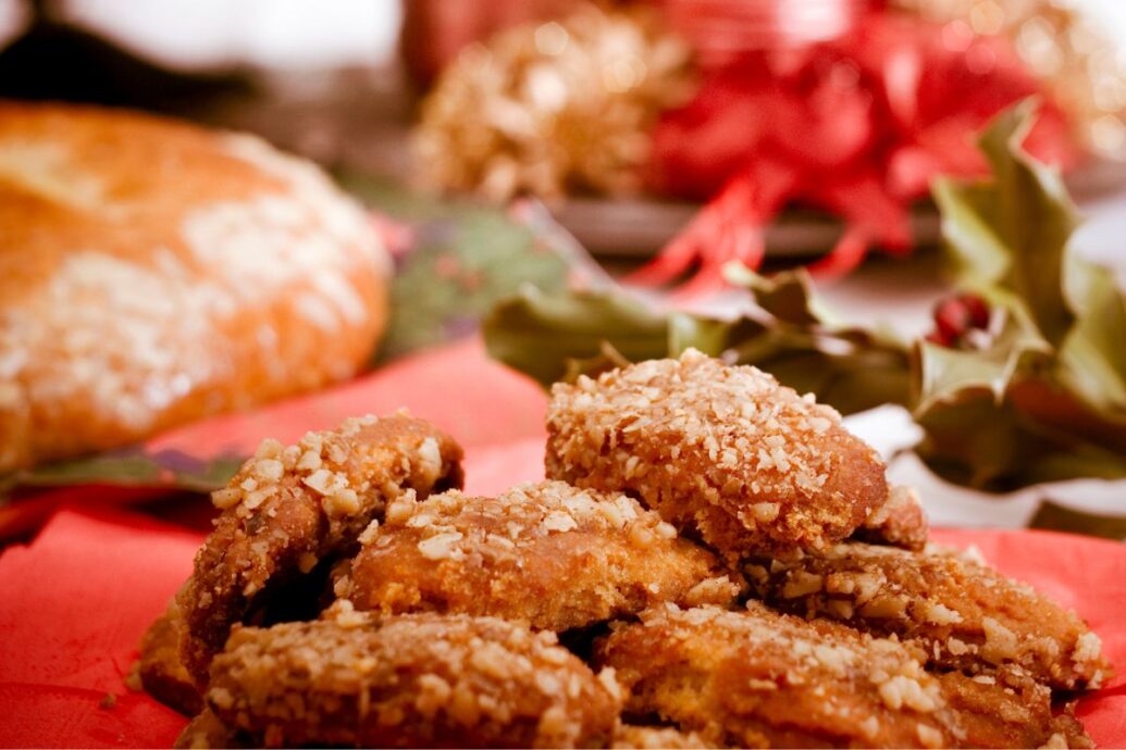 A festive plate of melomakarona, traditional Greek Christmas cookies topped with chopped walnuts, set against a holiday-themed background.