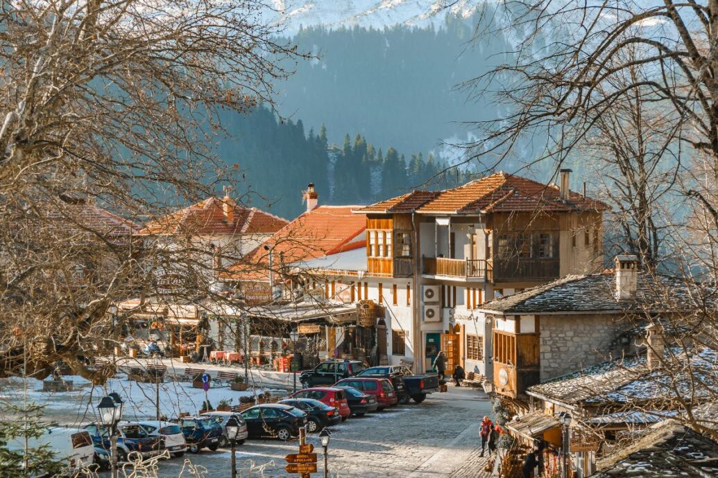 A charming winter village scene in Metsovo featuring traditional architecture, snow-dusted rooftops, and a backdrop of pine-covered mountains.