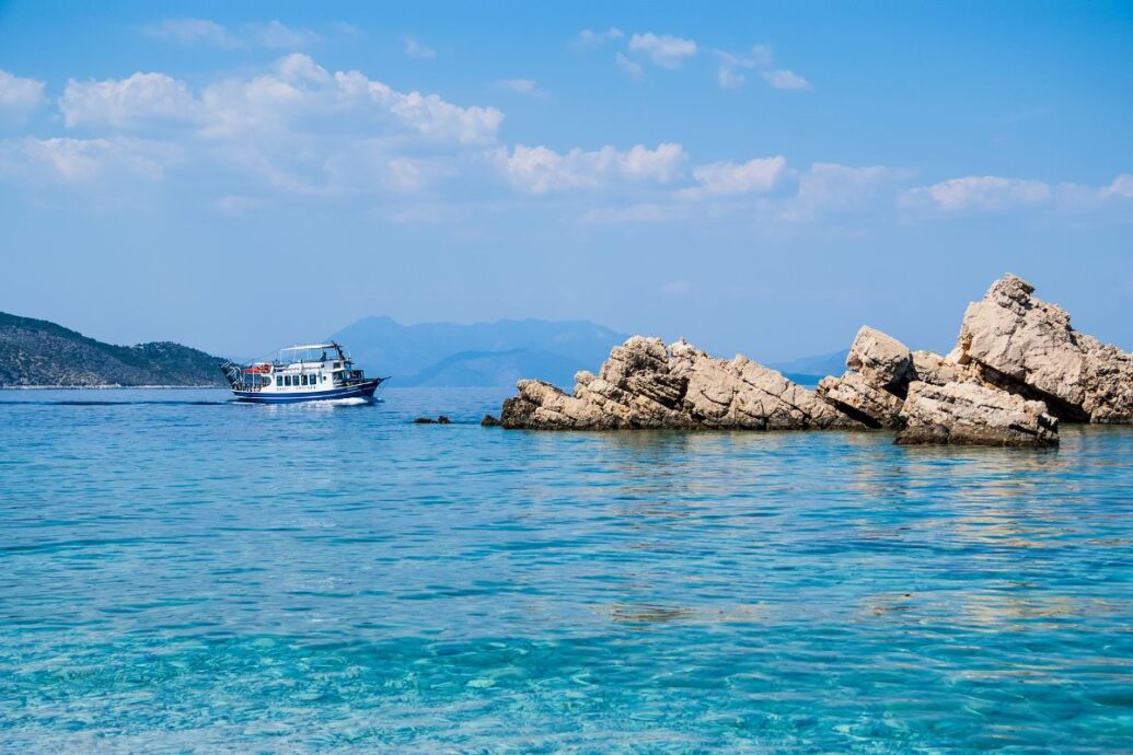 A serene coastal scene featuring clear blue waters, a rocky outcrop, and a small boat sailing in the distance under a bright sky.