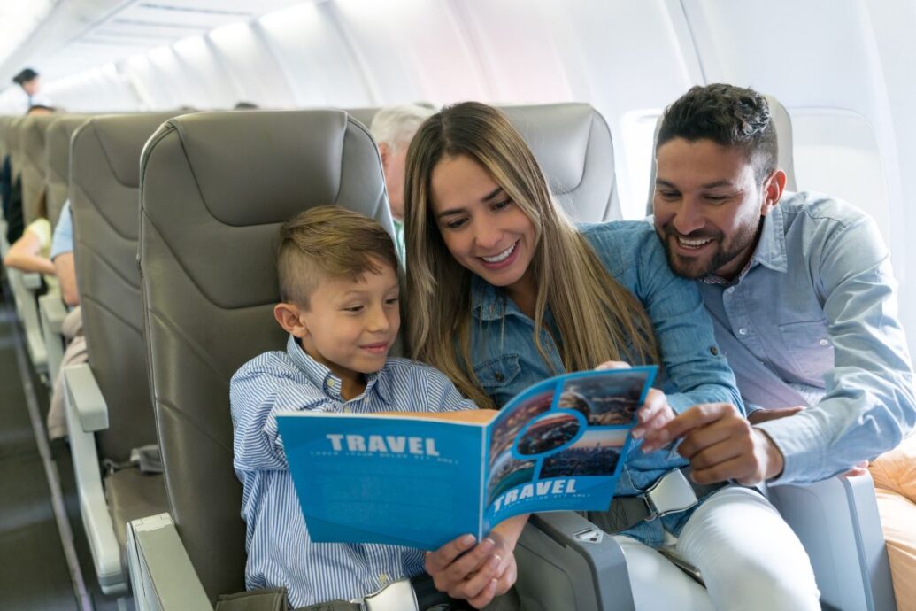 A smiling family sitting on an airplane, looking at a travel brochure together, creating a cheerful and engaging atmosphere.