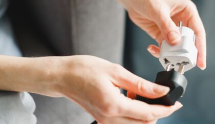 A person connecting a black plug to a white travel adapter, symbolizing preparation or practicality. Greece Travel Adapter