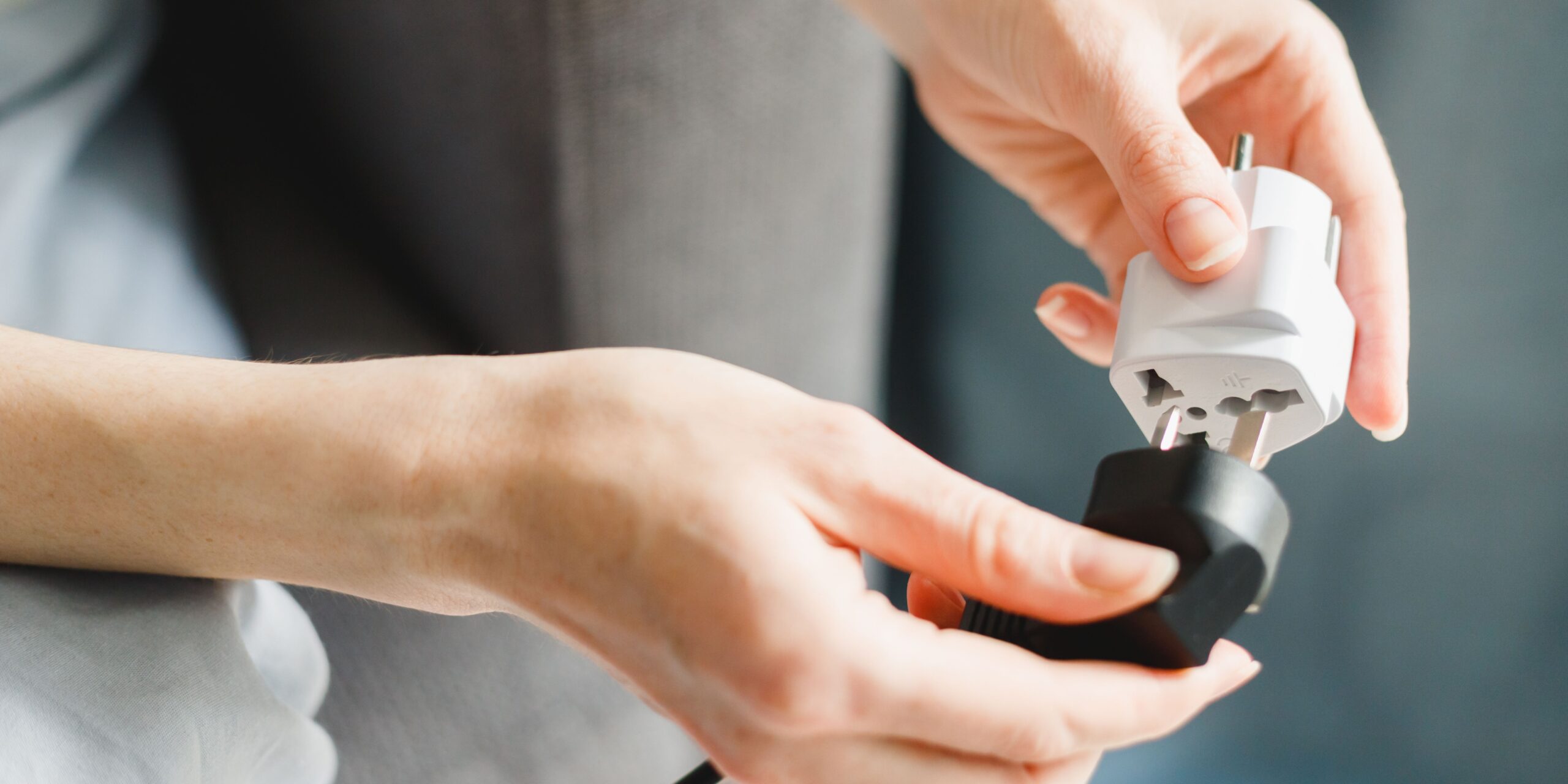 A person connecting a black plug to a white travel adapter, symbolizing preparation or practicality. Greece Travel Adapter