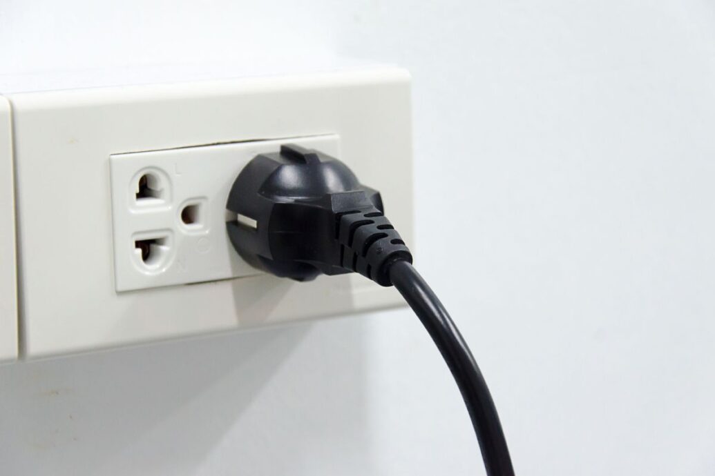 A black plug inserted into a white electrical socket on a wall.