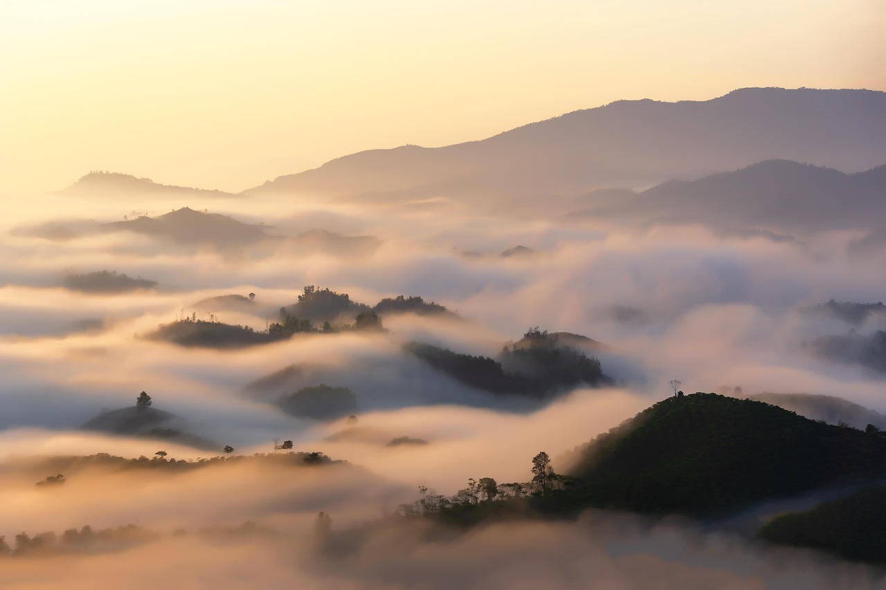 A picture of a sunset with mountains and clouds covering them.