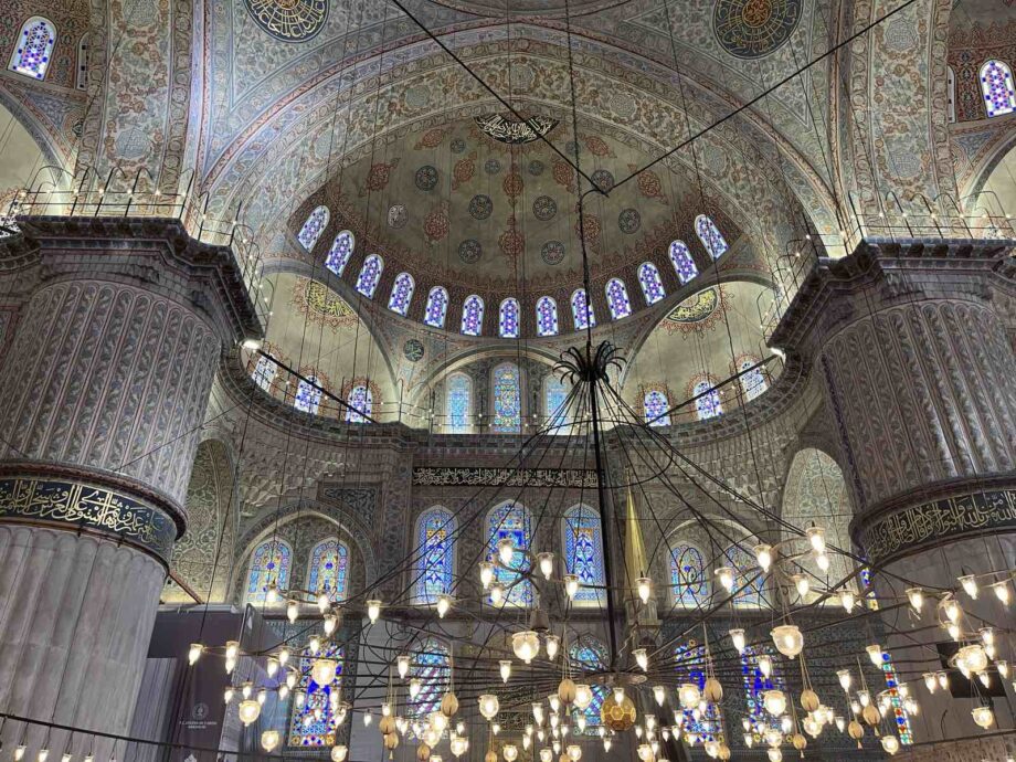 The interior of the Blue Mosque. Huge arches with painted blue and green details as well as tinted glasses with different hues of blue.