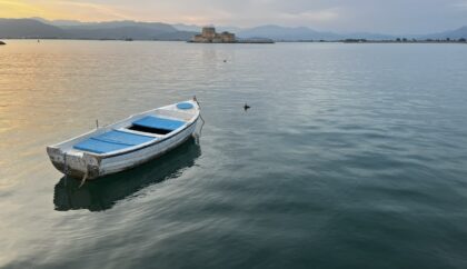 a picture of nafplio's bourtzi in the sunset wth a small white boat floating in front of it