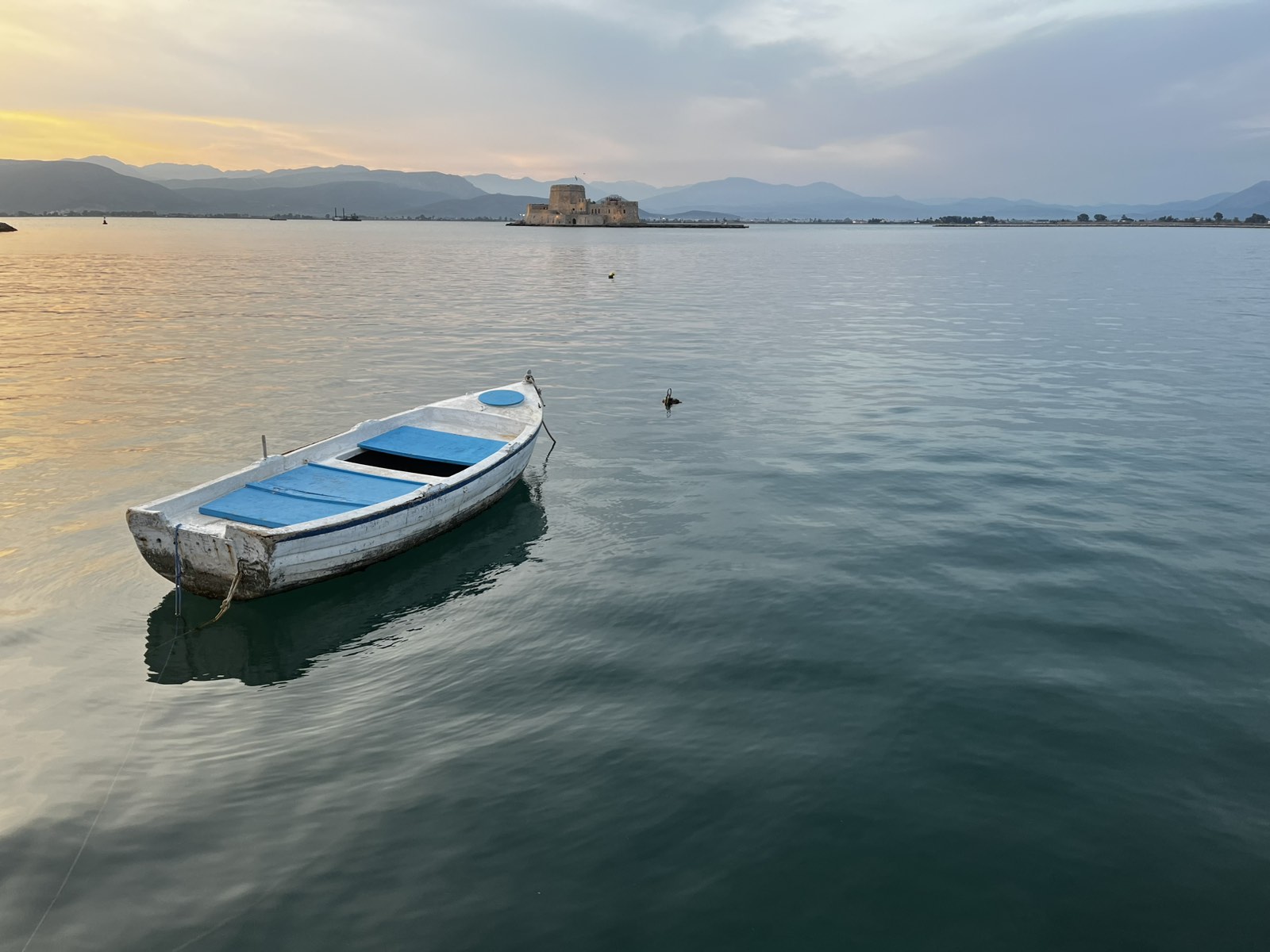a picture of nafplio's bourtzi in the sunset wth a small white boat floating in front of it